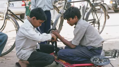 Bambini che riparano biciclette, India.