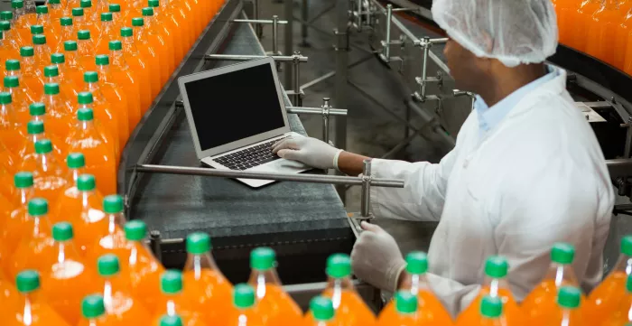 Male worker using laptop amidst production line in juice factory